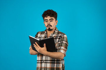 Young man stands on blue background and reading book