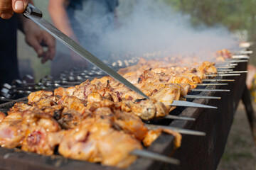 A barbecue cook cooks meat on skewers on a barbecue on the street