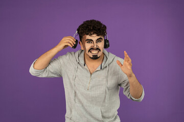 Portrait of handsome guy with creative makeup listening music with headphones and looks angry