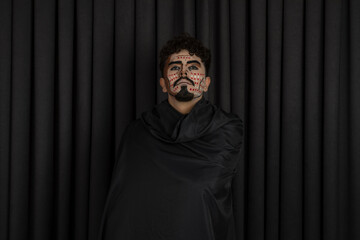 Confident young man with black cape stands on black background