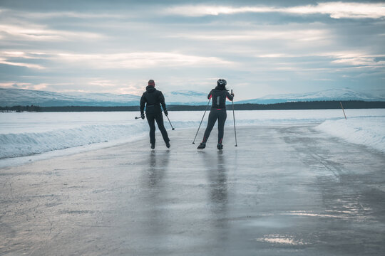 Two young women on ice skating track called "medvinden" on lake storsj&ouml;n near &Ouml;stersund (Sweden Lapland) skating with ski poles towards mountain view (Oviksfj&auml;llen).