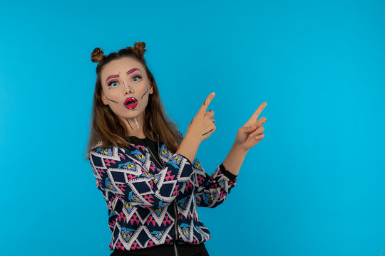 Portrait of attractive girl with creative makeup point fingers to the left side on blue background