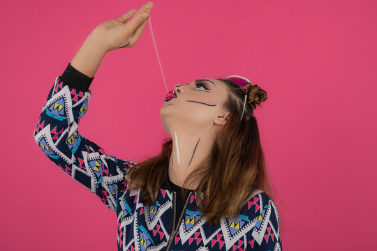 Close up portrait of young girl wearing creative makeup and stretching her gum on pink background