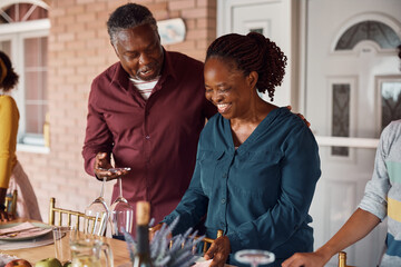 Happy senior black woman and her husband having fun while setting dining table for family lunch on...