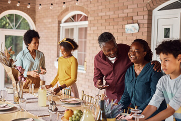 Happy senior African American man and his wife having fun while setting dining table for family meal on patio