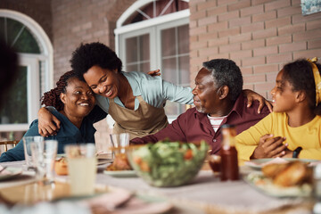 Happy black woman embracing her senior parents during family meal on patio.
