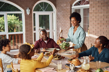 African American woman serving salad to her extended family during lunch at dining table on patio.