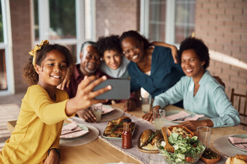 Fototapeta na wymiar Happy black multi-generation family taking selfie during lunch at dining table.