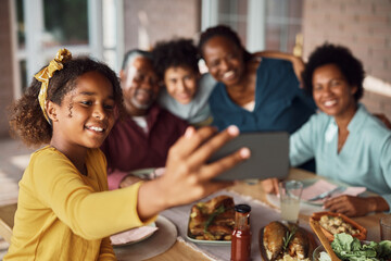Happy African American girl and her extended family taking selfie during meal on patio.