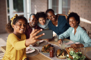Happy black multi-generation family taking selfie while gathering for lunch at dining table on patio.