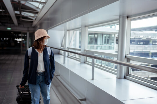 Traveler wearing protective mask with suitcase in airport concept.Young girl walking with carrying luggage and passenger for booking ticket flight at international vacation time in holiday.