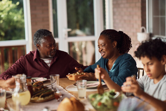 Senior Black Couple Talks During Family Meal At Dining Table On Patio.