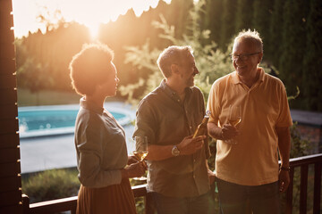 Happy senior man having a drink and talking to his son and black daughter in law on patio.