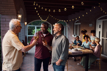 Group of multi-ethnic men toasting with drinks during family gathering on patio.
