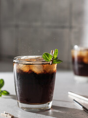 Cola or cuba libre cocktail in glass with ice cubes and mint and metal straws. Soft drink close up. Text space