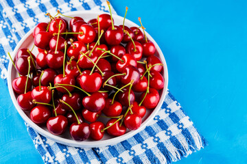 Sweet cherries on a white plate. Ripe cherries and a white-blue napkin on a blue background. Copy space