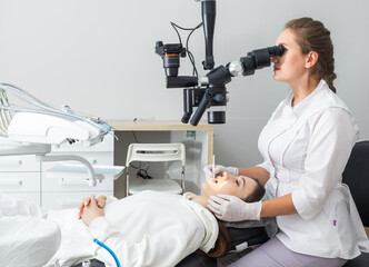 Female dentist using dental microscope treating patient teeth at dental clinic office. Medicine,...