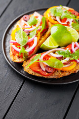 Healthy vegetarian toasts and lime on a black plate. Bruschetta with tomatoes, greens and olives. Healthy open sandwiches on black boards. Copy space. Top view