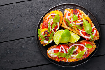 Healthy vegetarian toasts and lime on a black plate. Bruschetta with tomatoes, greens and olives. Healthy open sandwiches on black boards. Copy space. Top view