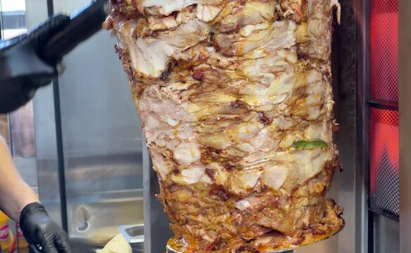 Cutting meat with a special knife from a vertically rotating skewer heated over medium heat and preparing portions of meat for shawarma (doner, gyros, doner kebab).