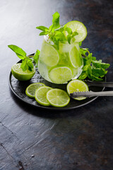 Mojito cocktail, mint and lime slices on a dark background. Summer cocktail mojito and ice tongs on a black plate. Top view. Copy space
