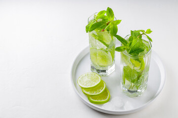 Mojito cocktail on a white background. Two glasses of mojito with mint and lime on a white plate. Summer drink concept. Copy space