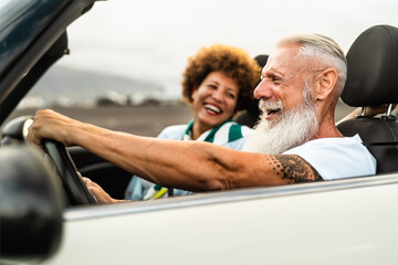 Happy senior couple having fun driving on new convertible car - Travel people lifestyle concept