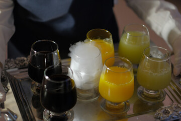 Silver tray with a variety of colored drinks being served at a party, one glass with dry ice producing white smoke.