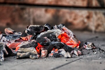 Charcoal Chimney Starter with fire making more embers inside the barbecue, with glowing charcoal embers next to it