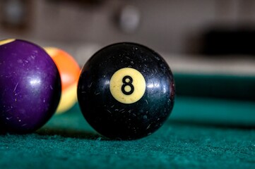 Black billiard ball with the number 8 on a green billiard table with other balls nearby.