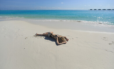 Fototapeta na wymiar sexy woman in a straw hat lies on the sea sand