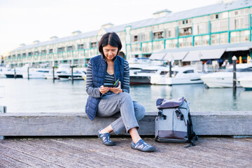 海の近くで座って携帯電話を確認する女性