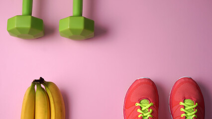Two dumbbells sneakers and three bananas on a light pink background. Healthy food and exercise concept. Space for text.