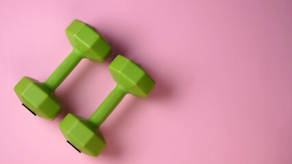 Beautiful green dumbbells for fitness on light pink background. Exercise active life concept. Space for text.