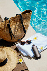 Swimming pool essentials concept. Beach bag with items for safe sunbathing on the deck, sunglasses,...