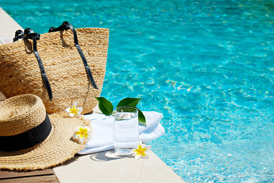 Swimming pool essentials concept. Beach bag with items for safe sunbathing on the deck, sunglasses, straw hat, white blanket & sunscreen product. Flat lay, copy space, top view, background.