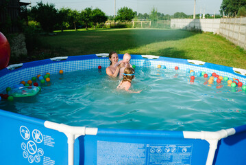 Family playing with balls toys in the swimming pool. Kids having fun in the pool. Summer leisure and holidays and vacation concept. People swim in a metal frame pool on a green grass lawn.