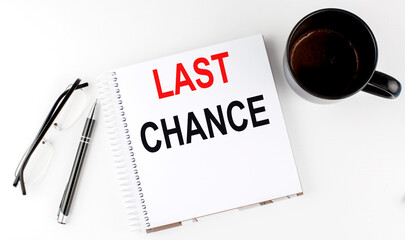 Coffee,glasses,pen and notebook written with LAST CHANCE , on white background.