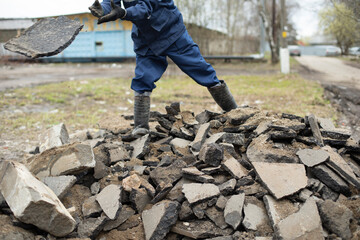 Worker collects stones. Guy cleans up construction debris. Broken asphalt.