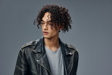 Serious adorable stylish tanned curly man leather jacket looks aside posing isolated on over gray studio background. Cool fashion offer. Huge Seasonal Sale New Collection concept. Copy space for ad