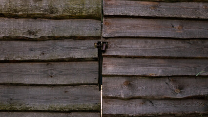 A fragment of a fence and a gate made of large wooden boards closed with a lock.