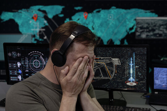 a military specialist with headphones covering his face with his hands. Concept: rocket launch, human surveillance, analytical center, criminal order.