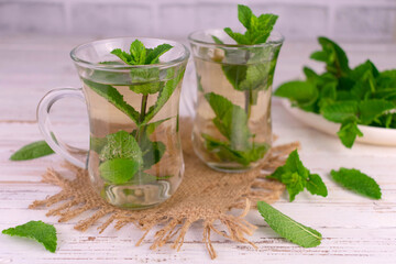 Mint tea in transparent cups on a white wooden background.
