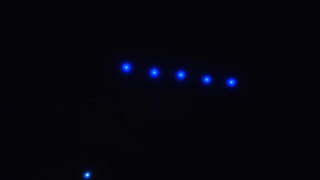 Bright colored lights move in rows in the night sky with theatrical smoke. Drone show