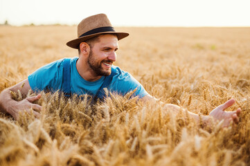 Naklejka na ściany i meble Young farmer enjoying and working in wheat field in warm sunny day.