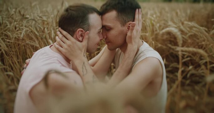 Close up two men gay hugging on field at the wheat smiling looking lovely at each other. Spending time together. Feel free and happy. LGBT Representatives. Slow motion.