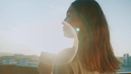 Close up attractive smiling young woman standing on her terrace, enjoying drinking tea feel happy watching views of sunrise landscape. Beautiful view. Slow motion