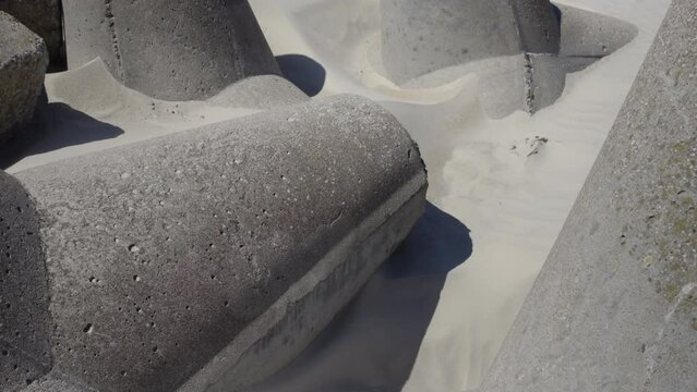 Concrete protective blocks against storm and erosion in sand. Sand in a strong wind swirls on the shore. Sunny summer day in Neringa. Lithuania
