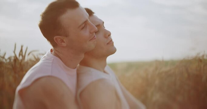 At sunlight two men gay hugging on field at the wheat smiling looking lovely at each other. Spending time together. Feel free and happy. LGBT Representatives. Slow motion.