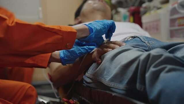 Male emergency medical team helps a sick person in an ambulance with saline hose.